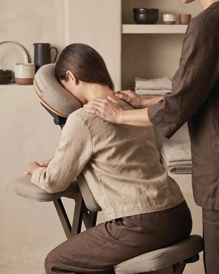 Nacken- und Schultermassage: eine Kundin sitzt vornübergebeugt im Massagestuhl
